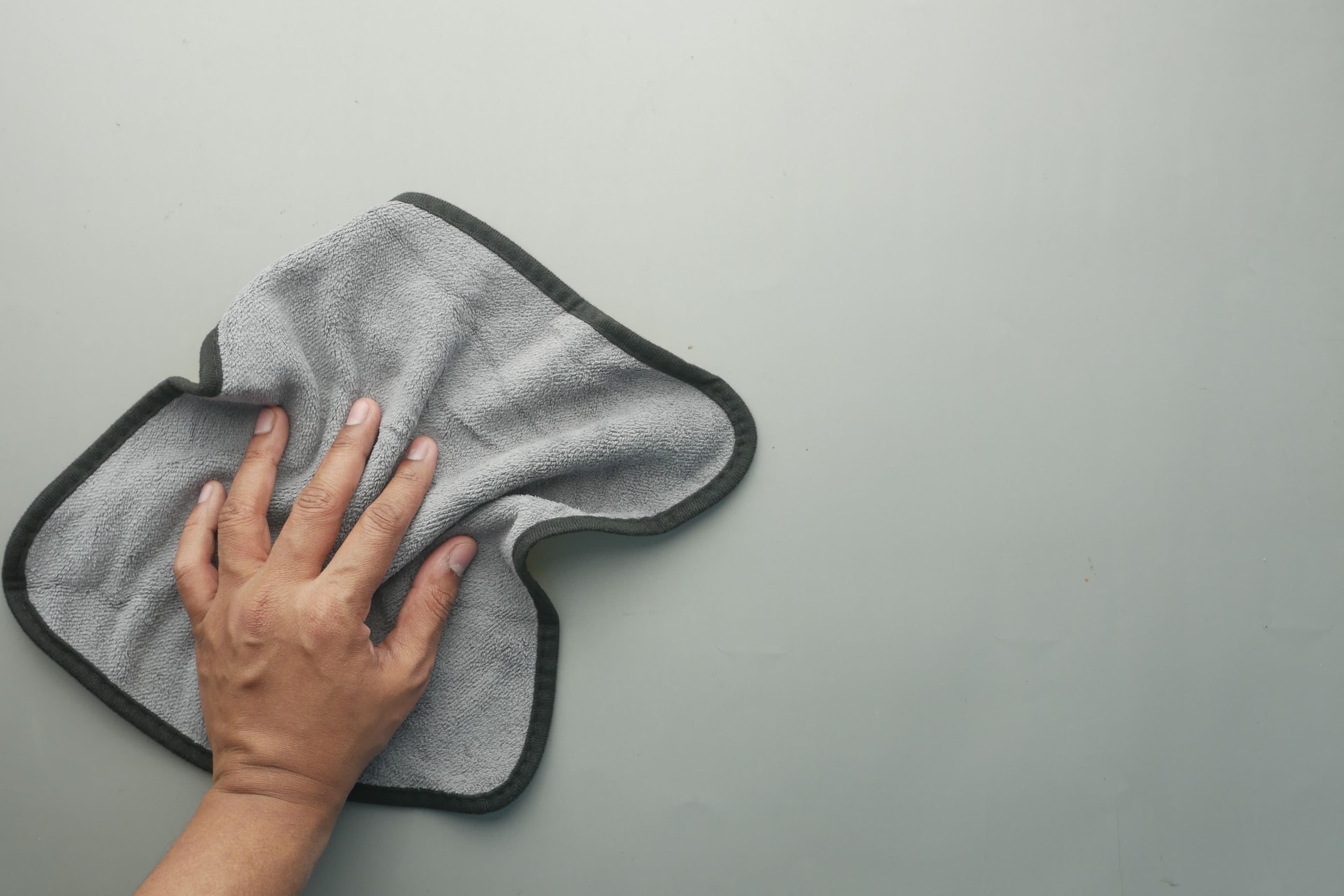 A hand wiping a pale surface with a gray microfiber cloth